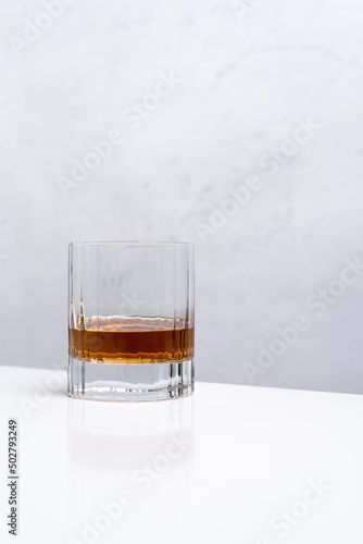 Un vaso de whisky sobre una mesa blanca y fondo claro 