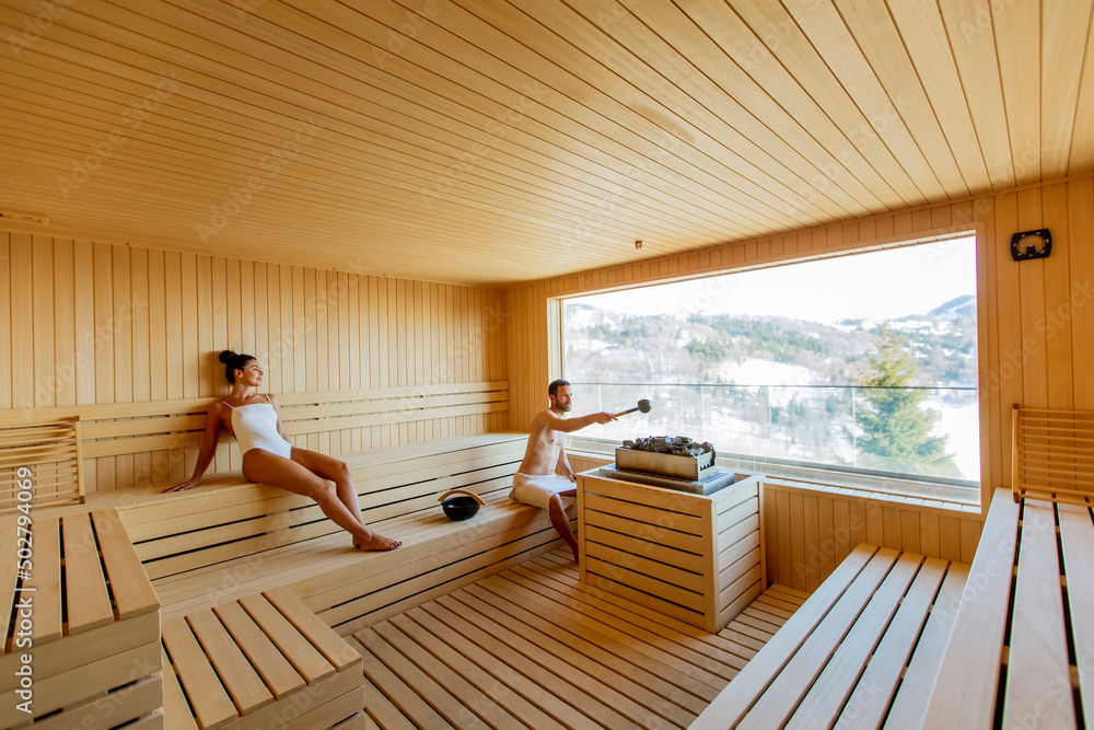 Young couple relaxing in the sauna and watching winter forest through the window Young couple relaxing in the sauna and watching winter forest through the window