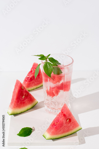 Un vaso de zumo de sandía con trozos de sandia y hielo sobre fondo claro 