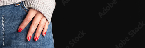 Obraz na plátně Female hand with beautiful manicure - red nails on jeans denim textile and black background with copy space banner