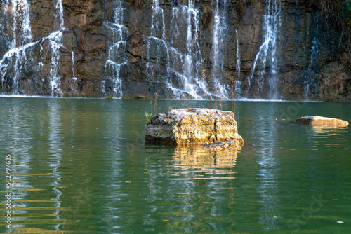 The view of a rock in green water while waterfall is in progress.