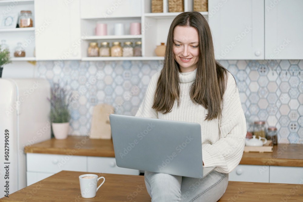 © yurolaitsalbert - young woman using laptop sitting on kitchen table .