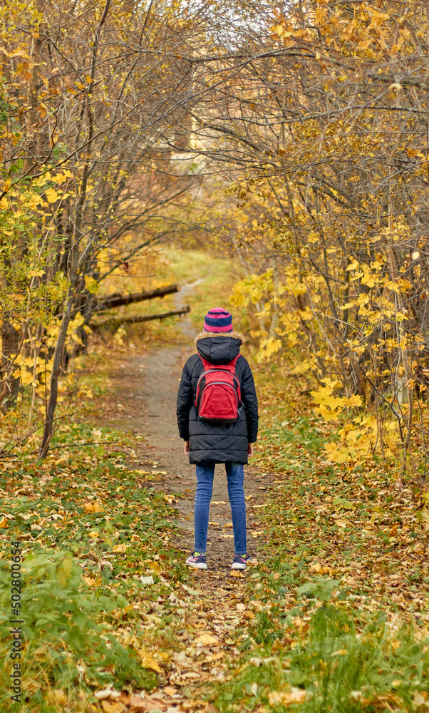 Little girl on the autumn path in the middle of autumn trees. Girl in a black jacket, jeans, hat and red backpack. Beautiful autumn. Little girl on the autumn path in the middle of autumn trees. Girl in a black jacket, jeans, hat and red backpack. Beautiful autumn.