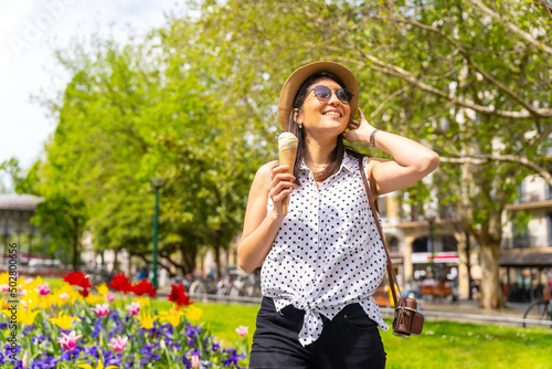 A tourist woman visiting the city eating an ice cream cone, enjoying summer vacations and with a camera, solo female traveler concept, wearing sunglasses