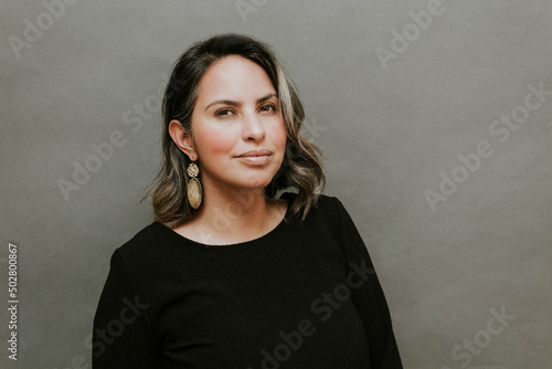 Middle aged hispanic woman standing in front of gray background with inspiring look