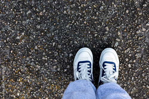A pair of white sneakers stand on the pavement, a photo of a selfie from top.