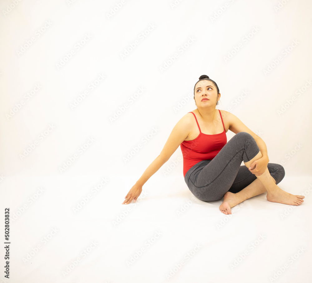 pretty woman in gray sportswear, red blouse, sitting concentrated, head up and holding one leg, on white background pretty woman in gray sportswear, red blouse, sitting concentrated, head up and holding one leg, on white background