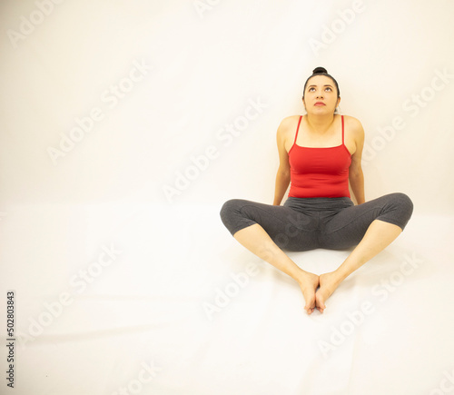 pretty athletic asian woman in gray sportswear, red blouse, sitting meditating after exercising with feet together, on white background