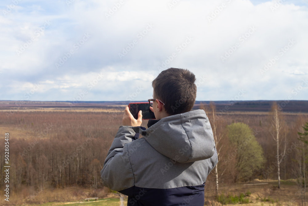 A teenage boy takes pictures on a smartphone of the landscape of a swamp in spring or autumn A teenage boy takes pictures on a smartphone of the landscape of a swamp in spring or autumn