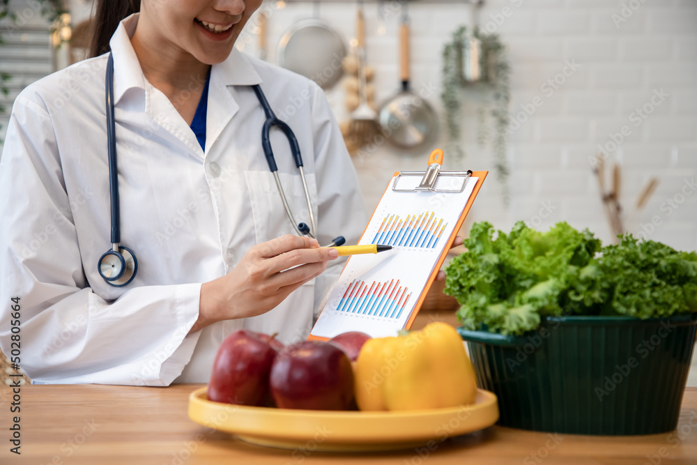 Nutritionist holding schematic vegetables graph plan for diet with various healthy products in the kitchen. Weight loss and right nutrition concept. Nutritionist holding schematic vegetables graph plan for diet with various healthy products in the kitchen. Weight loss and right nutrition concept.