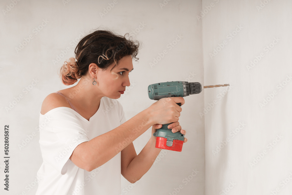 A young woman drills a wall with an electric drill. A young woman drills a wall with an electric drill.