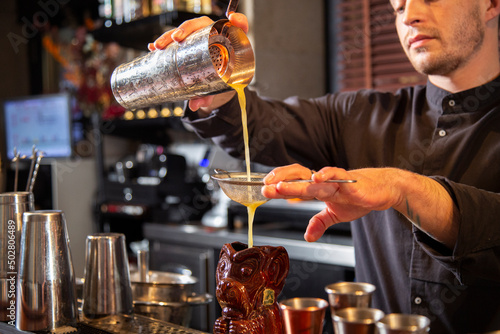 Crop barman pouring cocktail through strainer into tiki glass in bar photo