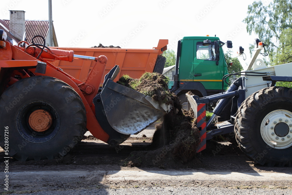 Two heavy bulldozers loads land with a scrapers on tipper truck background. Earthworks. landscaping. construction site. Asphalt laying