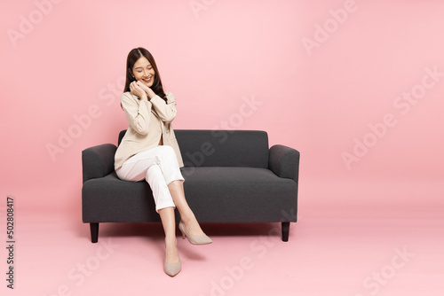 Canvas Print Excited Asian businesswoman sitting on sofa isolated on pink background