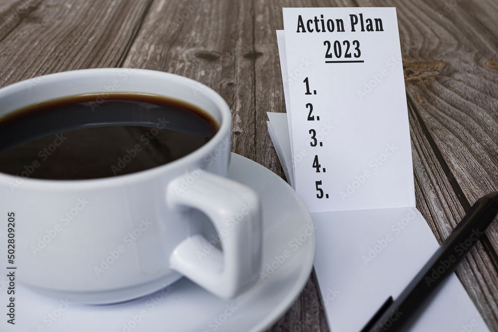 Note book with action plan 2023 text and coffee on wooden desk. Note book with action plan 2023 text and coffee on wooden desk.