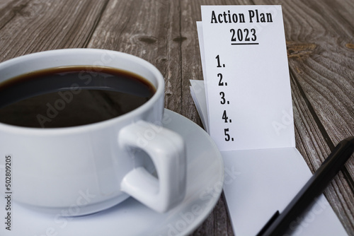 Note book with action plan 2023 text and coffee on wooden desk.