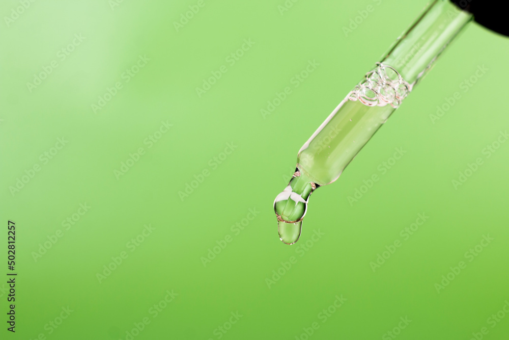 Dripping essential oil or serum from pipette on green background macro image. Eco, natural cosmetics concept, selective focus, close up image