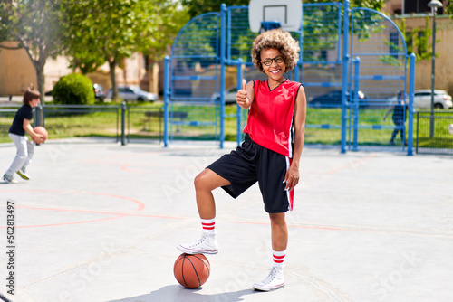 girl with afro hairstyle with a ball on a basketball court © JENOCHE