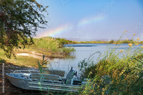 A small motor boat rests on the shore of Livingstone Island in Zambia  rainbow on the horizon from Victoria Falls