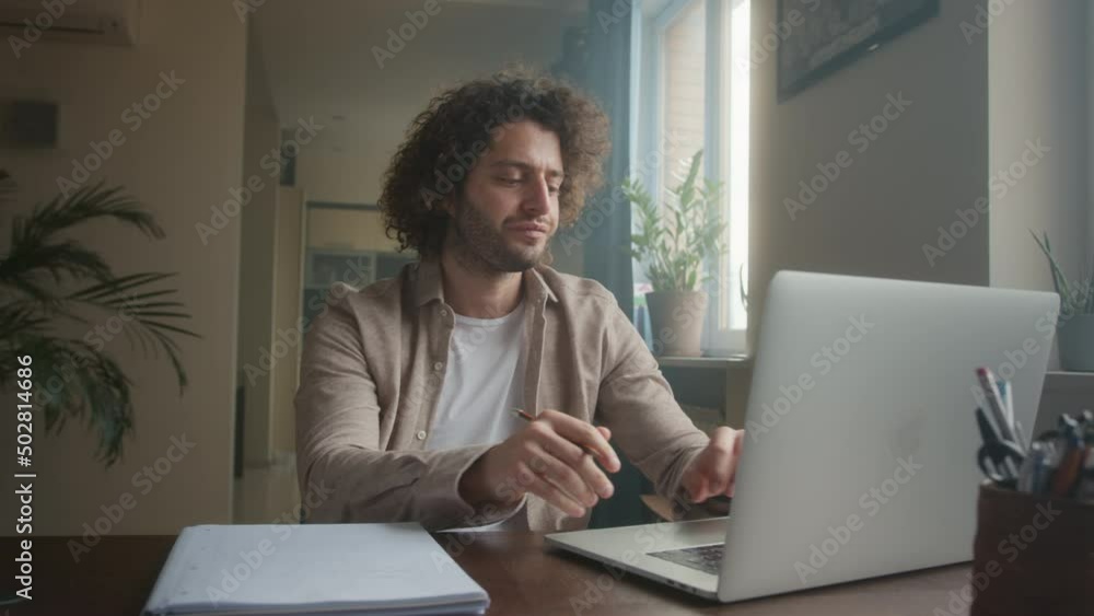 Professional Creative Man Sitting at His Desk in Home Office Studio Working on a Laptop. Man working with Data and Analyzing Statistics. Camera Moving Around Professional Creative Man Sitting at His Desk in Home Office Studio Working on a Laptop. Man working with Data and Analyzing Statistics. Camera Moving Around