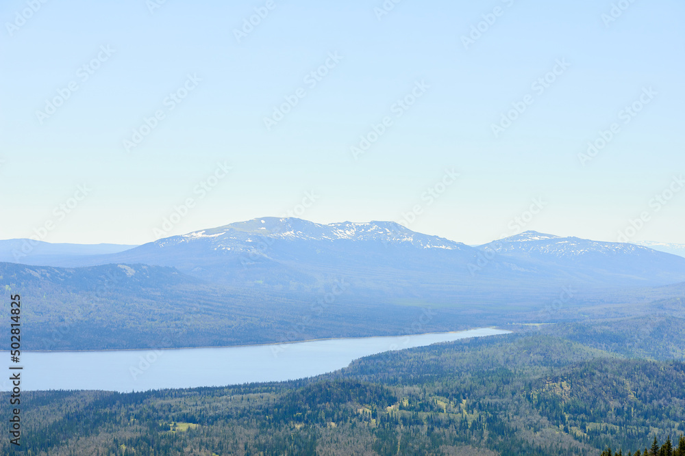 Aerial view of vast woodland, wide river and stunning mountains with snowcaps in the distance. National park, Ural region, Russia Aerial view of vast woodland, wide river and stunning mountains with snowcaps in the distance. National park, Ural region, Russia