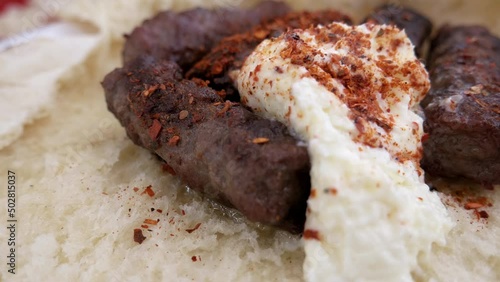Cevapi - a traditional minced meat dish from the grill, served on a bun with creamy kaymak and paprika powder. Close up, macro, handheld shot  photo
