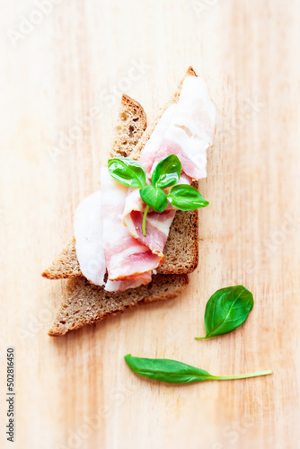 Food. Sandwiches. Rye bread with bacon slice and basil leaf on wooden background
