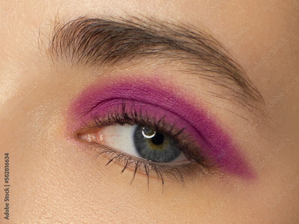 Obraz premium Glamour close-up portrait of beautiful woman model face with winged purpule eyeliner make-up, clean skin on white background. Long eyelashes and thick eyebrows.