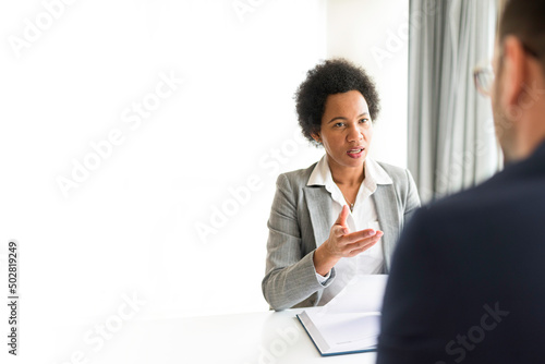 Businesswomen talking to client in her office. African American HR manager sitting at desk in office talking with a potential new employee during job interview. Copy space