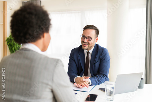 Handsome HR manager interviewing young African-American women job applicant in the office. Confident businessman consulting client at meeting, business conversation