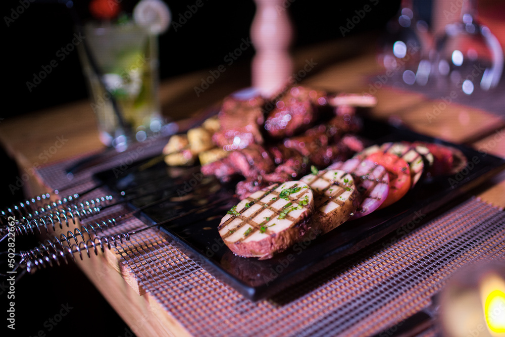 A plate of Chicken and beef BBQ with grilled tomatoes, potatoes and onions A plate of Chicken and beef BBQ with grilled tomatoes, potatoes and onions