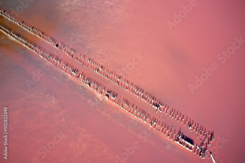 Aerial view of the salty red lake with old wooden beams sticking out of the water with salt growths. Shooting from a drone.
