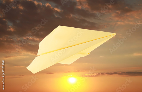 Yellow paper plane and view of beautiful sky at sunset