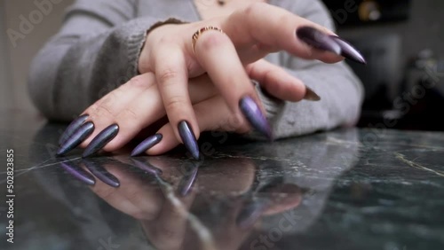 close-up of a female hand with long black nails impatiently tapping her fingers on a reflective black surface. photo