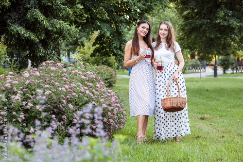 Two beautiful fashionable women in polka dot clothes spending time together outdoors in summer, drinking cocktails and having picnic. photo