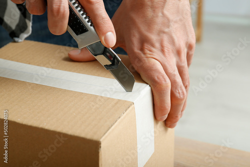 Man using utility knife to open parcel indoors, closeup