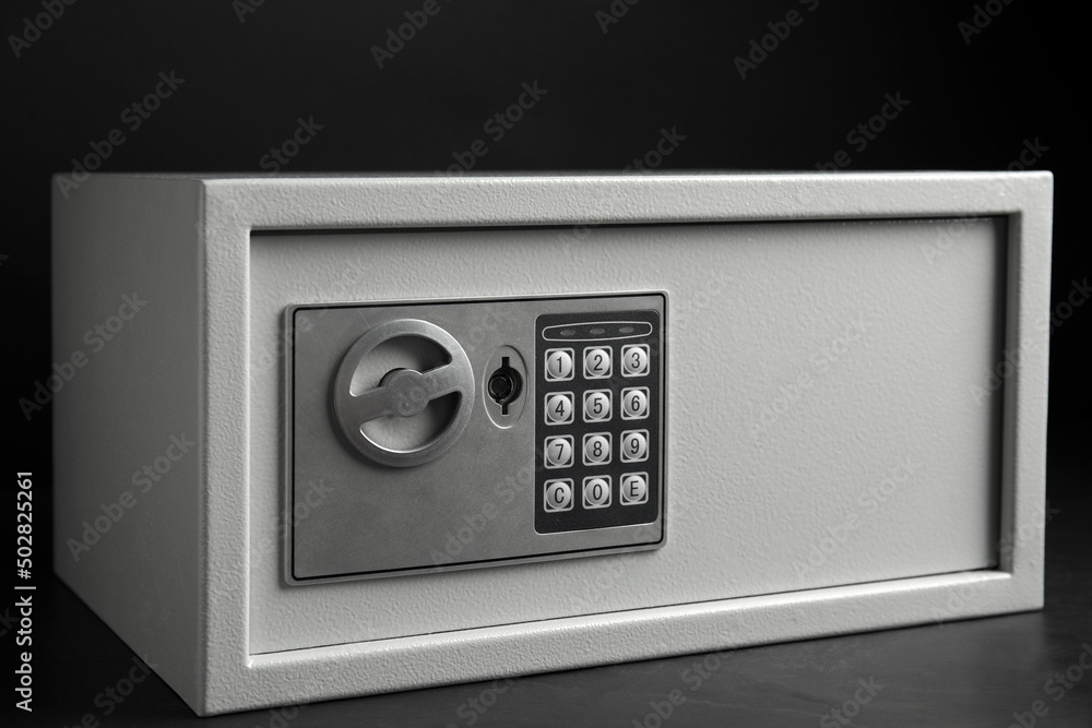 Steel safe with electronic lock on grey table against black background, closeup view Steel safe with electronic lock on grey table against black background, closeup view