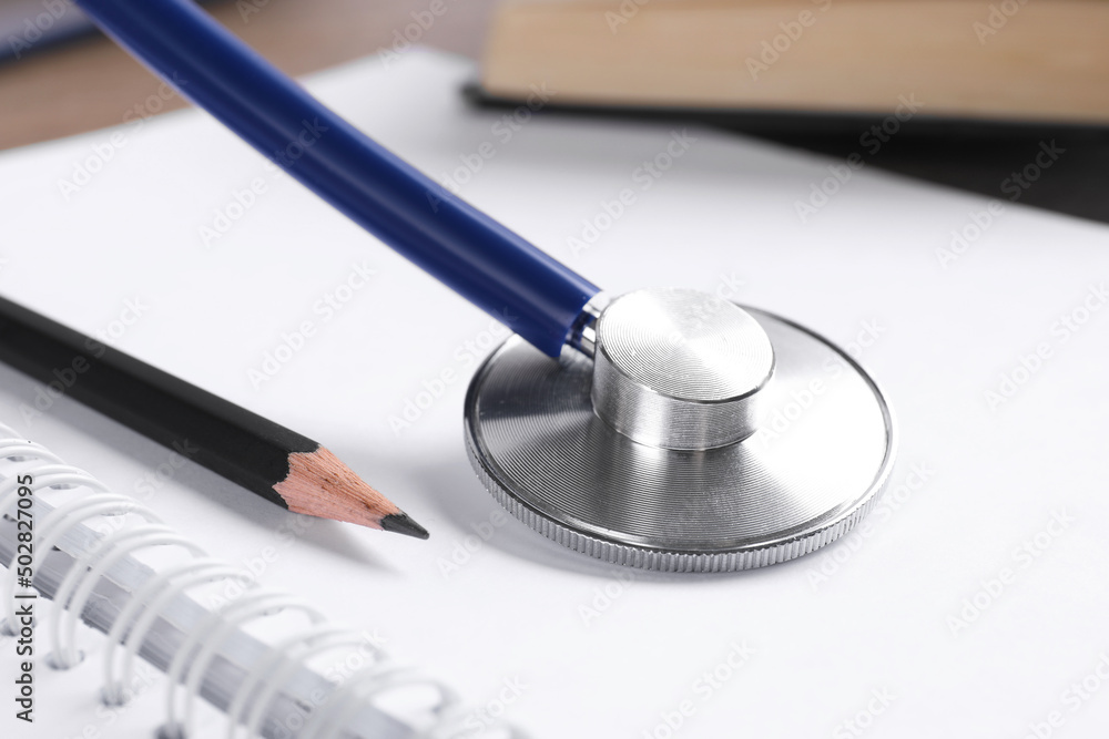 Student textbook, blank notebook, pencil and stethoscope on table, closeup. Medical education Student textbook, blank notebook, pencil and stethoscope on table, closeup. Medical education