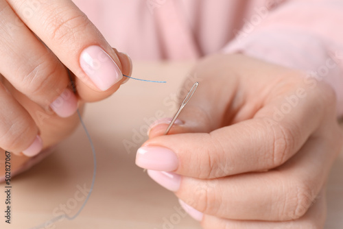 Woman threading sewing needle at table  closeup