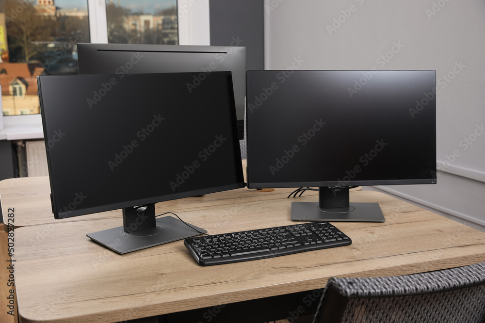 Modern interior. Workplace with multi-monitor on wooden desk in office, space for text Modern interior. Workplace with multi-monitor on wooden desk in office, space for text