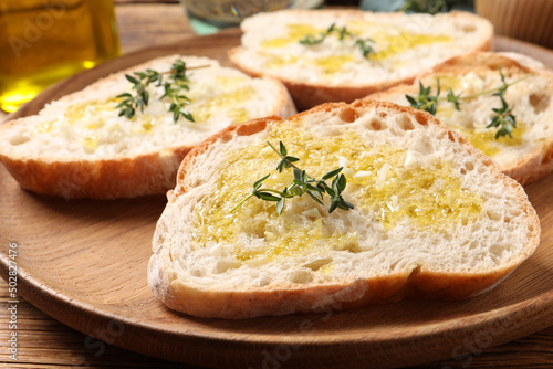 Tasty bruschettas with oil and thyme on wooden plate, closeup