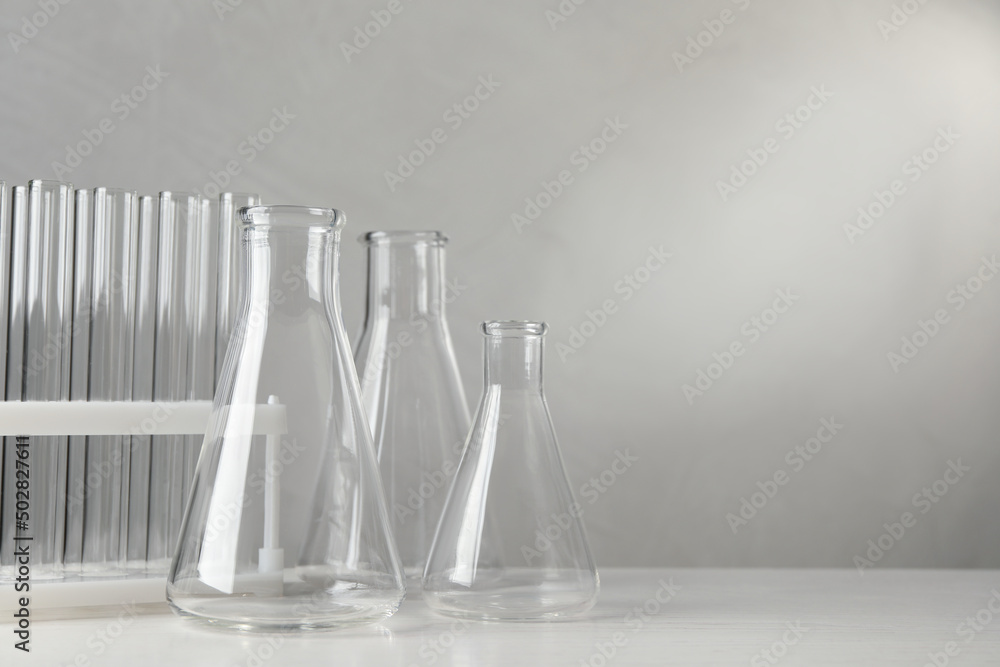Set of laboratory glassware on white table against grey background, space for text Set of laboratory glassware on white table against grey background, space for text