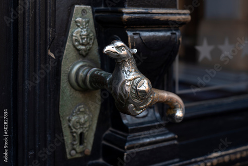 Old door handle. Wooden vintage entrance door with antique door handles in the shape of bird. Selective focus