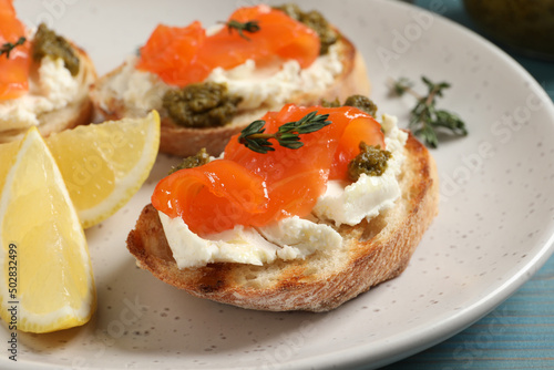 Delicious bruschettas with cream cheese, salmon and pesto sauce on light blue wooden table, closeup