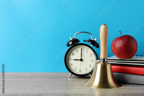 Golden school bell, apple, alarm clock and books on wooden table against turquoise background, space for text