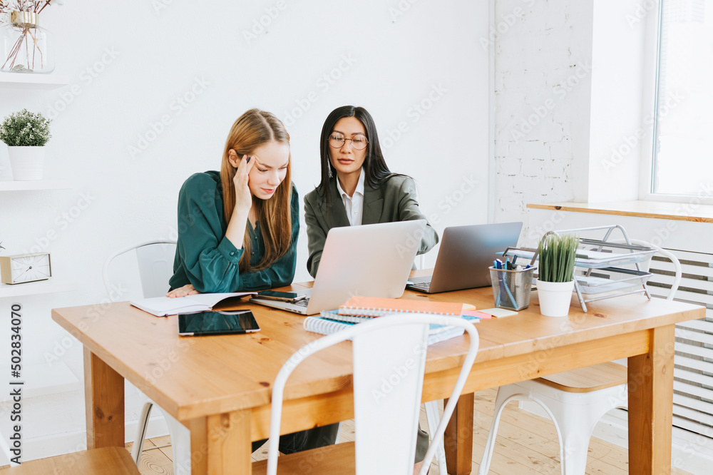 two young business women professionals in formal wear clothes work in modern office using laptop, tablet, brainstorm and search for solutions together, confident independent Asian girl solves problems two young business women professionals in formal wear clothes work in modern office using laptop, tablet, brainstorm and search for solutions together, confident independent Asian girl solves problems