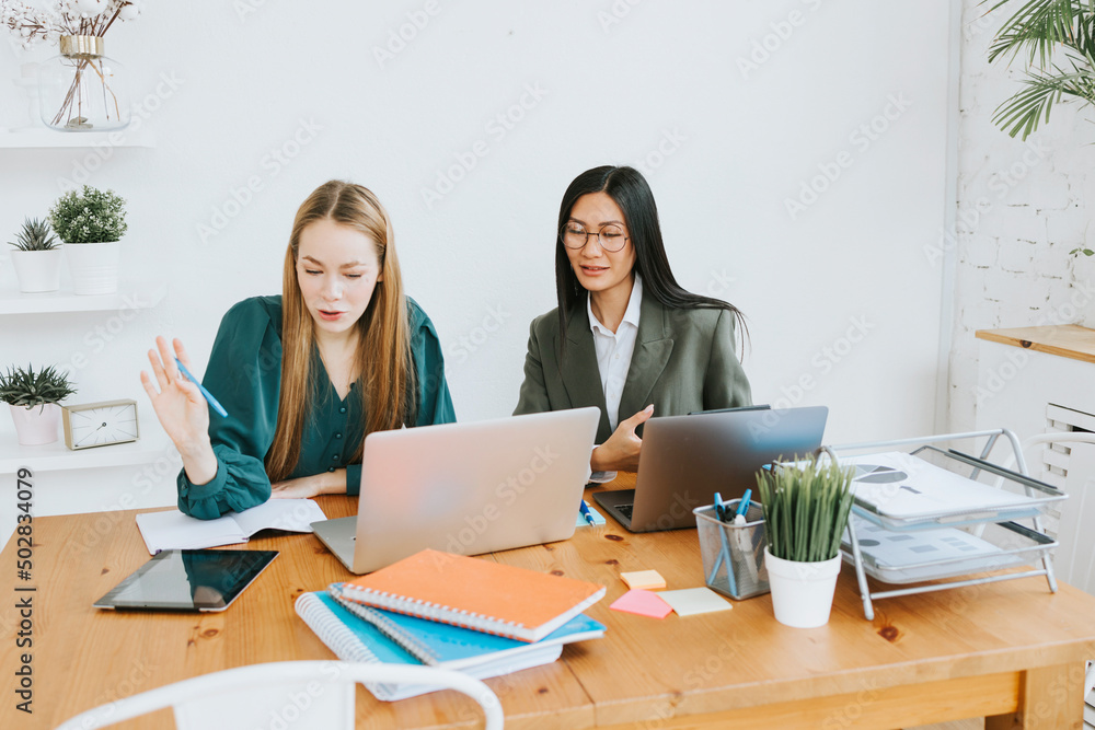 two young business women professionals in formal wear clothes work in modern office using laptop, tablet, brainstorm and search for solutions together, confident independent Asian girl solves problems two young business women professionals in formal wear clothes work in modern office using laptop, tablet, brainstorm and search for solutions together, confident independent Asian girl solves problems