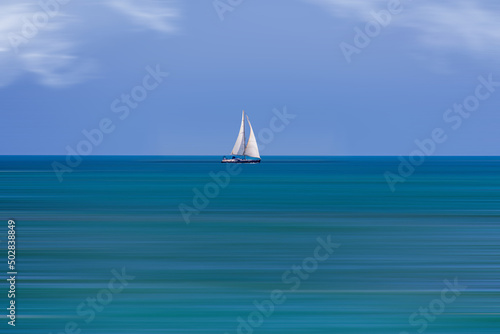  calm sea landscape with white sailboat against blue sky and long water time