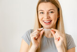 Smiling young woman over white background holding an invisible braces aligner recommending this new treatment. Dental healthcare concept.