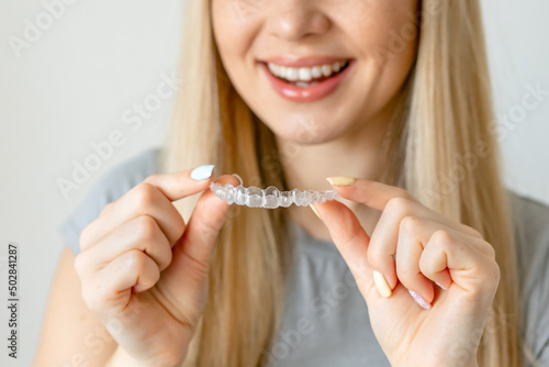 Close up of clear aligners in hands of happy girl who is standing and showing orthodontic device to the camera. Selective focus and isolated background